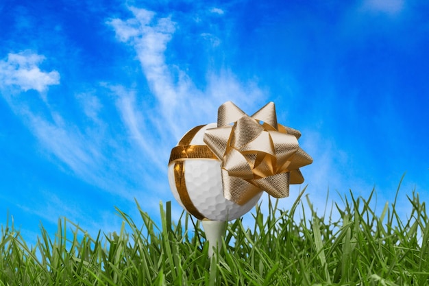 Golf ball on tee with golden ribbon and bow