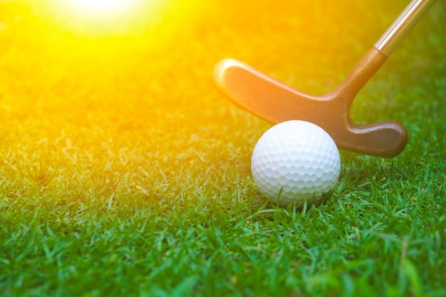 Golf balls and clubs are placed on the lawn.Golf club hitting a white golf ball with green grass.