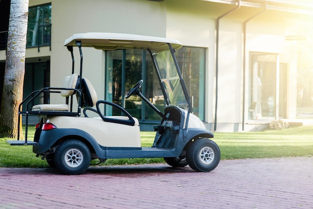 Golf cart is parked near the modern cottage house. Electric car in the parking lot of  resort area