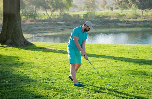 Golf club man is standing on the green grass of the lawn on a golf field on a warm evening