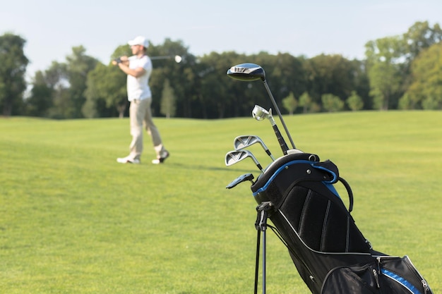 Golf equipment Golf clubs in golf bag on the foreground man playing golf on the background during summer vacation