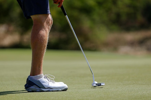 Golf player legs at golfing ball hole Golfer posing on green lush course