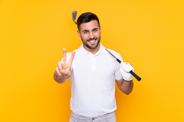 Golfer player man over isolated yellow wall smiling and showing victory sign