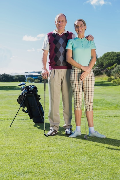 Golfing couple standing smiling at camera on a sunny day at the golf course