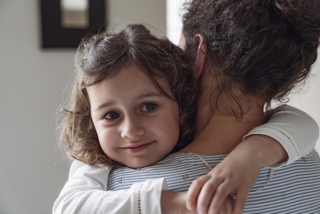 Good family mother and daughter Little daughter hugging her mom with a smile looking at the camera at home