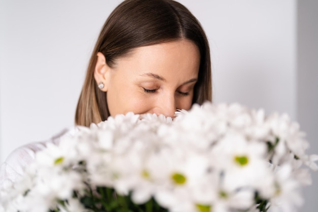 Good looking Caucasian woman smells flowers she is happy for get a fresh bouquet of white chrysanthemum