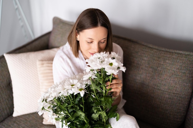 Good looking Caucasian woman smells flowers she is happy for get a fresh bouquet of white chrysanthemum