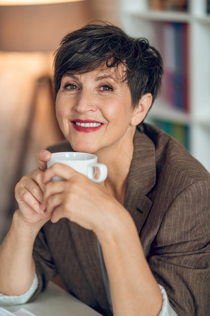 Good-looking dark-haired woman sitting at the table with a coffee mug in hands