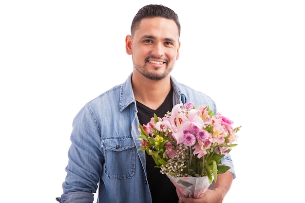 Good looking Latin guy holding a bunch of pink flowers and getting ready to meet his date for dinner