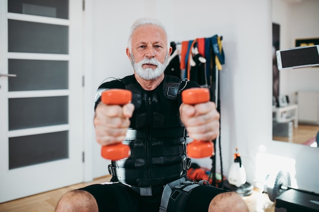 Good looking and positive senior man doing exercises in electrical muscular stimulation suit