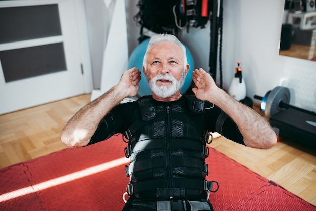 Good looking and positive senior man doing exercises in electrical muscular stimulation suit