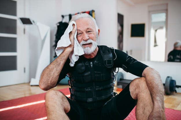 Good looking and positive senior man doing exercises in electrical muscular stimulation suit