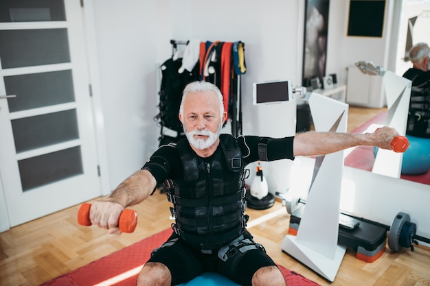 Good looking and positive senior man doing exercises in electrical muscular stimulation suit.