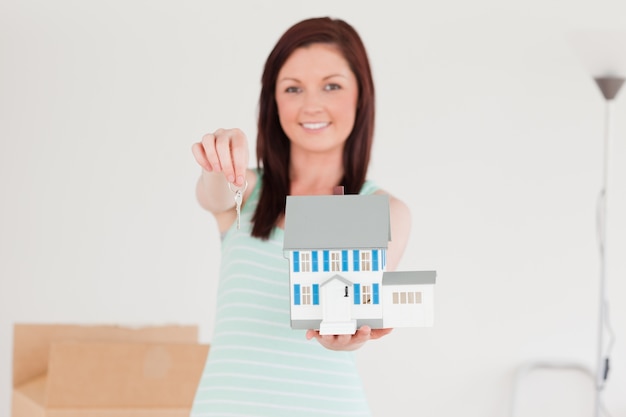 Photo good looking red-haired female holding a miniature house while standing on the floor