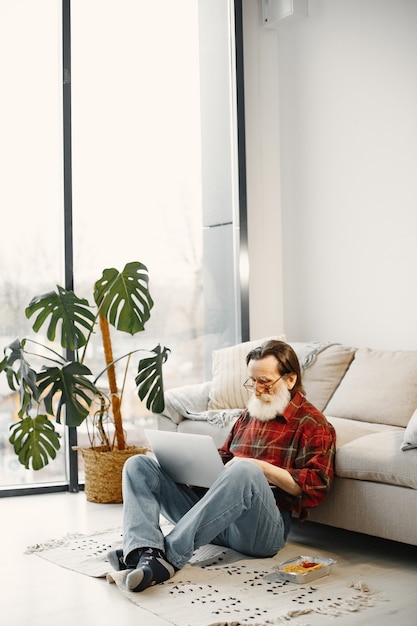 Good-looking senior man. Working with laptop. Sitting on the floor. Eating fast food.