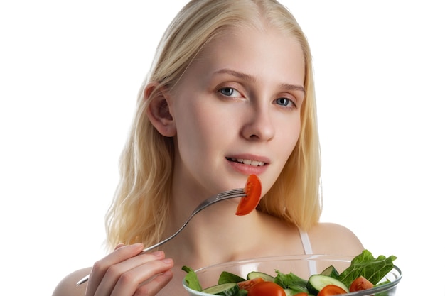 Good looking woman eating a bowl of salad while standing against a white wall.