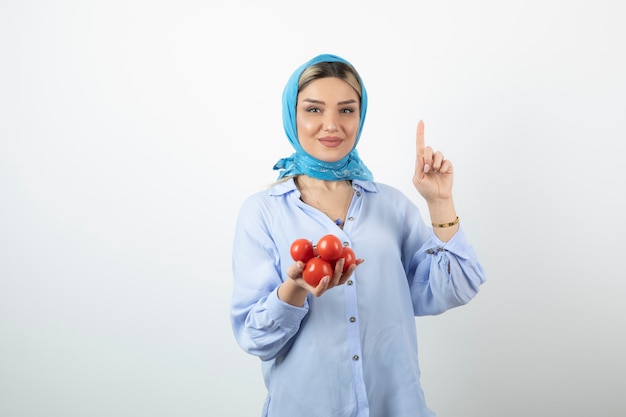 Good-looking woman in shawl showing number one with hand and holding red tomatoes