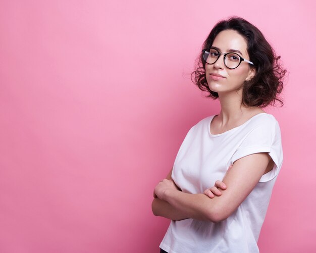 Good looking young Caucasian woman in round transparent eyewear, keeps hand raised, dressed in casual outfit, 