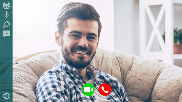 Photo good looking young man in casual wear looking at camera and smiling while having video call