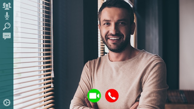 Good looking young man in casual wear looking at camera and smiling while having video call