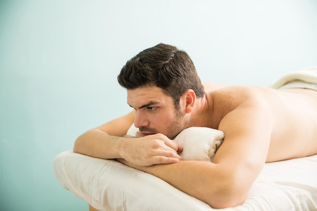 Good looking young man lying on a massage bed in a spa and waiting for his therapist to begin