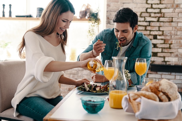 Good meal in a good company. Beautiful young couple enjoying healthy breakfast while sitting in the kitchen at home