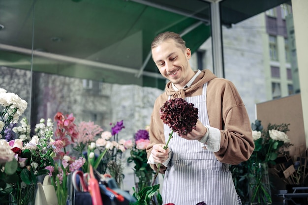 Good mood. Cheerful young man keeping smile on his face while looking at flower