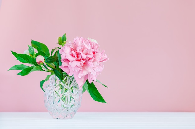 Good morning. Pink peonies in a crystal vase on a pink wood background, copy space, close up.