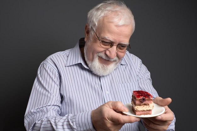 Good-natured smiling man  holding a plate and looking at the cake