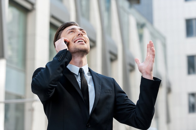 Good news. Cheerful young men in formalwear talking on the mobile phone and rise his hand up