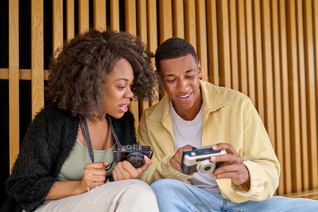 Good photo. Smiling african american young man showing camera to interested curly woman sitting chatting outdoors in good mood