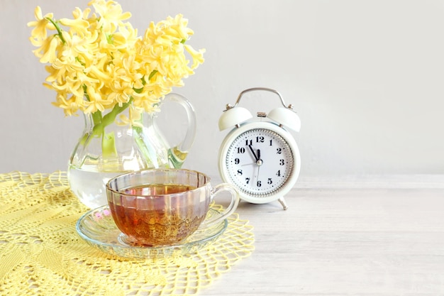 Good spring day a bouquet of yellow hyacinths a white alarm clock a cup of tea on a yellow openwork napkin on a gray background closeup space for text