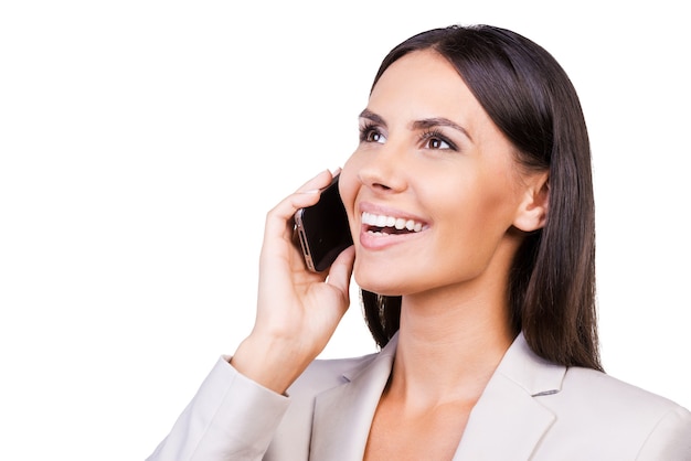 Good talk. Confident young businesswoman in suit talking on the mobile phone and smiling while standing isolated on white background