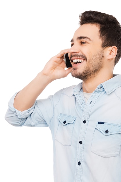 Good  talk. Portrait of cheerful young man talking on the mobile phone and smiling while standing against white background