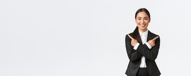 Goodlooking asian saleswoman suggest two choices Attractive businesswoman in black suit pointing fingers sideways have few variants help make decision standing white background