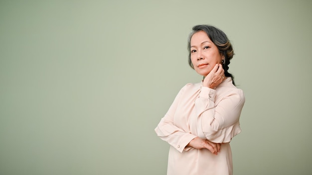 Gorgeous 60s agedasian woman arm crossed hand on chin looking at camera isplated background