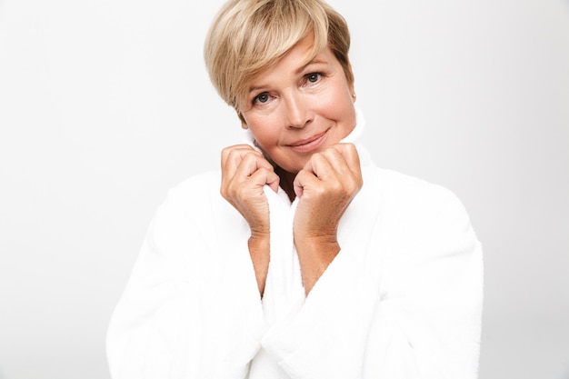  gorgeous adult woman with short blond hair wearing white housecoat looking  isolated over white wall