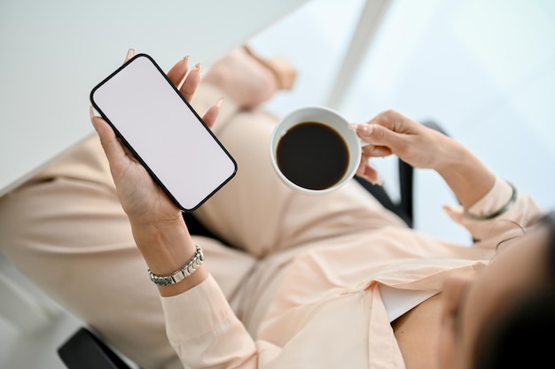 Gorgeous Asian businessman sipping coffee while using her smartphone at her desk top view