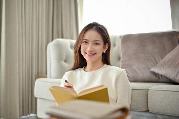 Gorgeous Asian woman sits in modern minimal living room holding a book or novel