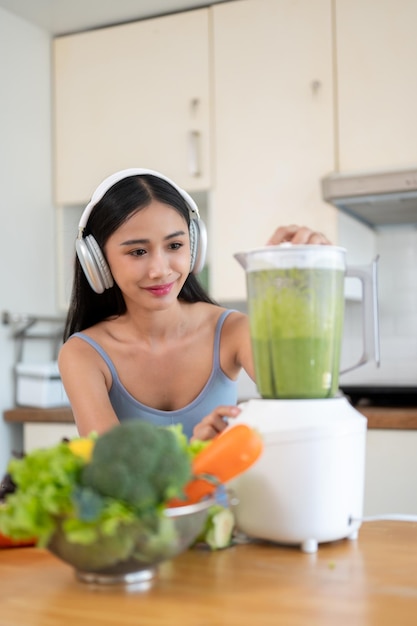 A gorgeous Asian woman in sportswear is making her healthy green detox smoothie in the kitchen