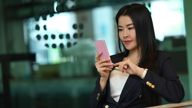 Gorgeous asian working woman sitting in office and using mobile phone