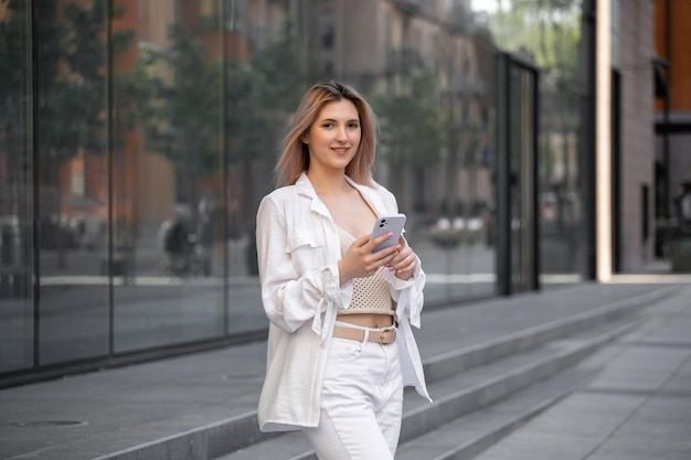 Gorgeous beautiful young woman with blonde hair messaging on the smartphone at the city street background pretty girl having smart phone conversation on city street