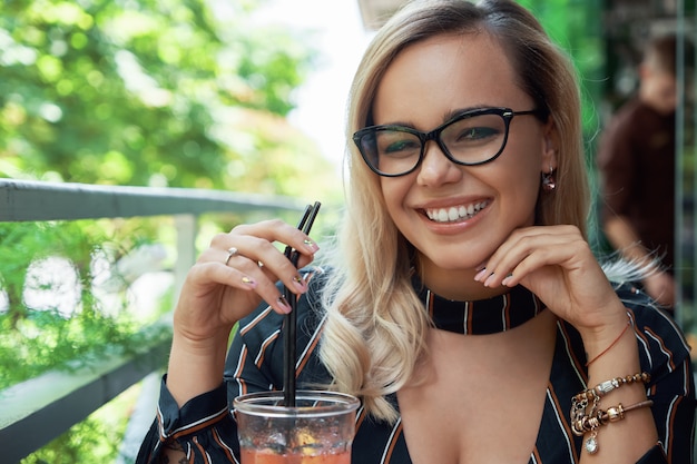 Gorgeous blond fashion woman with wavy hair resting on cafe terr