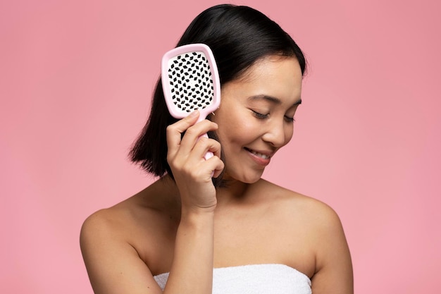 Gorgeous brunette asian woman brushing hair with modern brush isolated