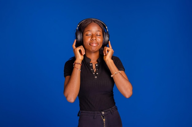 Gorgeous brunette lady listening music in headphones and singing on blue background