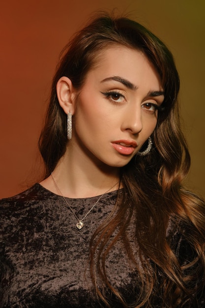 Gorgeous brunette lady in stylish jewelry and black velvet dress posing against colorful background