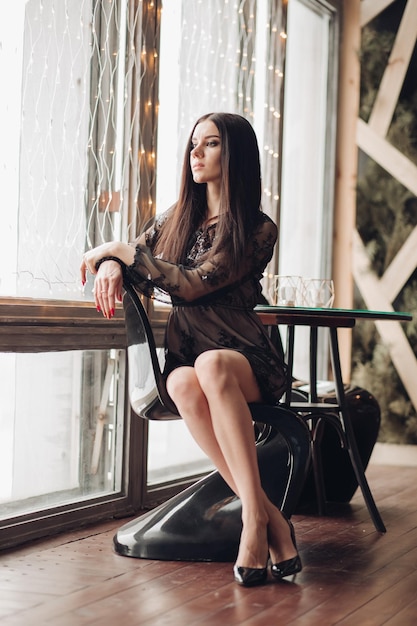 Gorgeous brunette model in black dress and heels in armchair