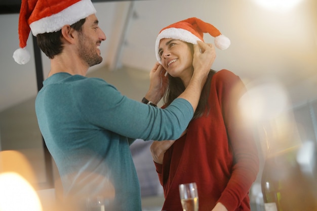  Gorgeous couple celebrating Christmas at home with champagne and Santa hats                             