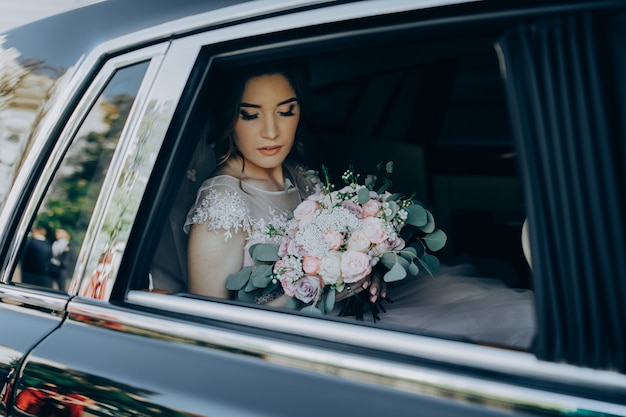 Gorgeous elegant bride posing in stylish luxury black car, sitting inside in saloon holding bouquet. luxury wedding.