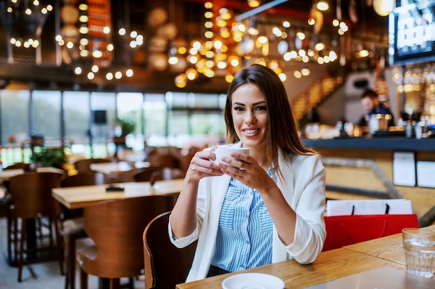 Gorgeous fashionable caucasian brunette with beautiful smile sitting in coffee shop